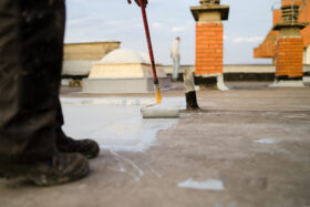 Low angle view of the worker putting the waterproofing coating on the roof of high building